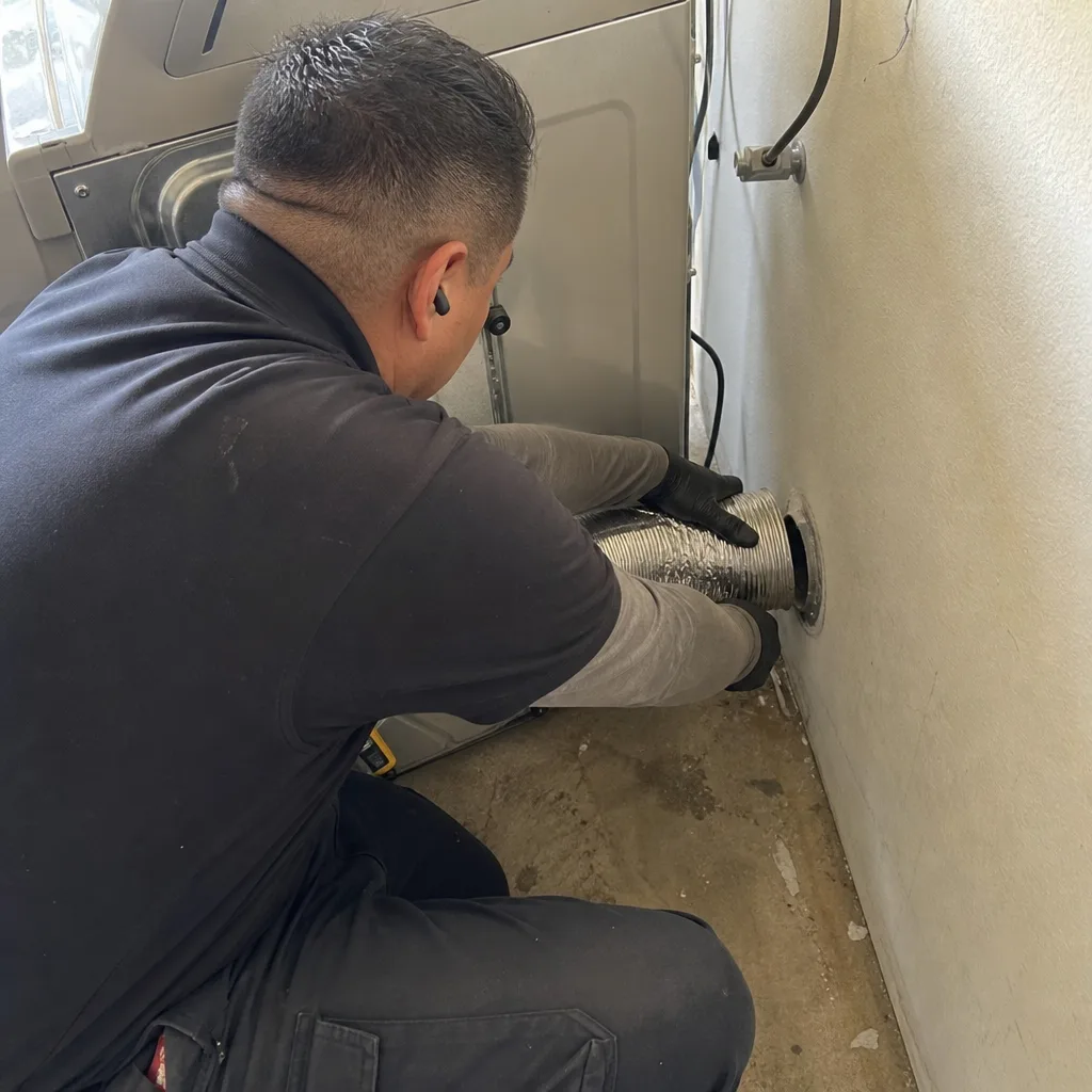Technician connecting a flexible dryer vent hose to a wall exhaust.